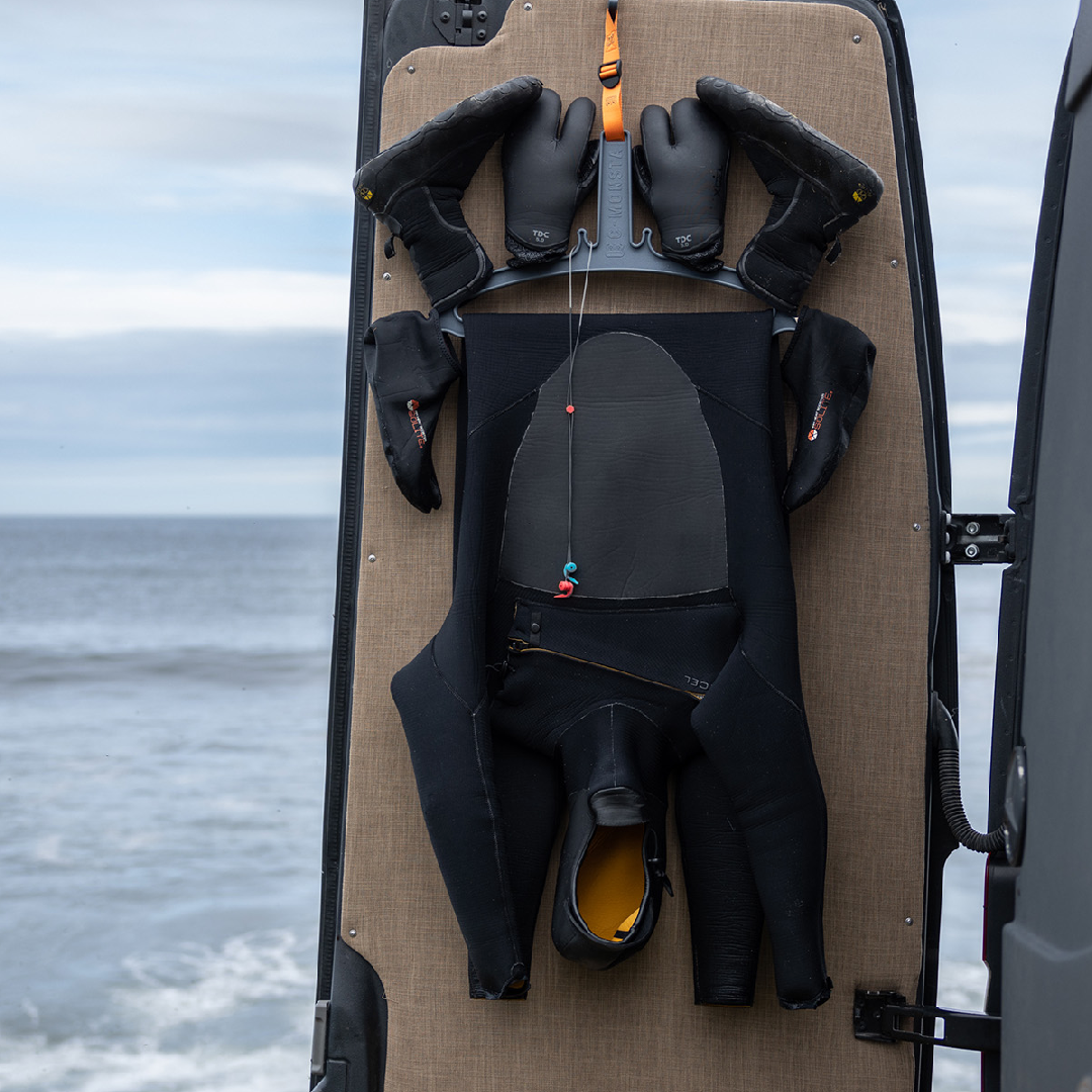 Surfing gear organizer holding wetsuit, gloves, and boots on a van door by the ocean | C-MONSTA.